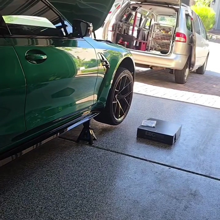 Green BMW raised on stands in a customer garage with the mobile service van parked behind