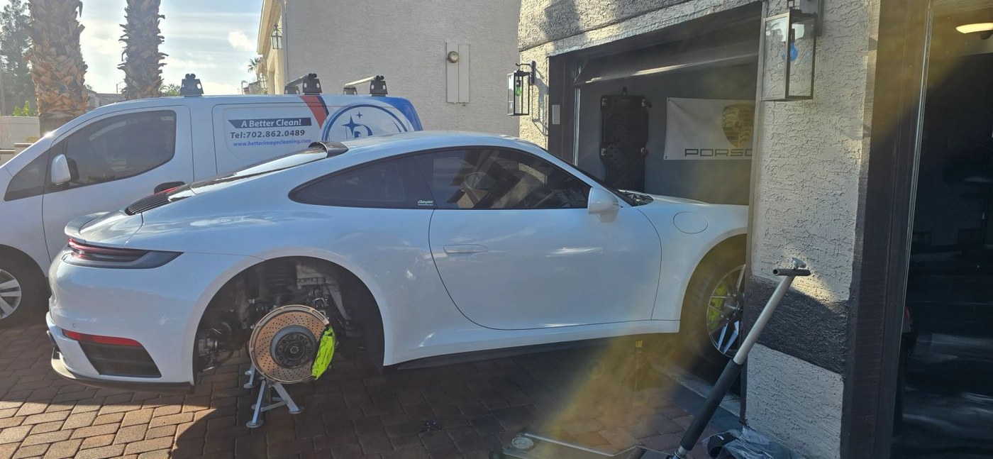White Porsche 911 with the wheel off for brake work in a customer driveway